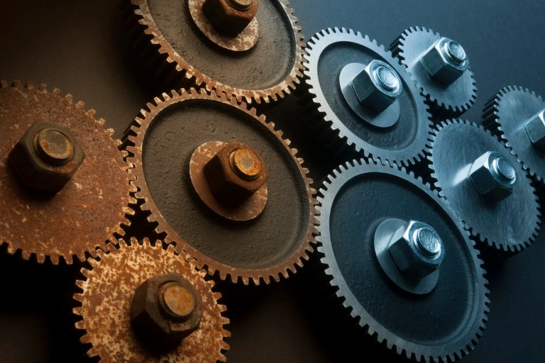 Four corroded rusty gears contrasting with new chrome gears.