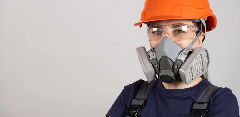 Woman in face mask, orange hardhat, and full PPE.