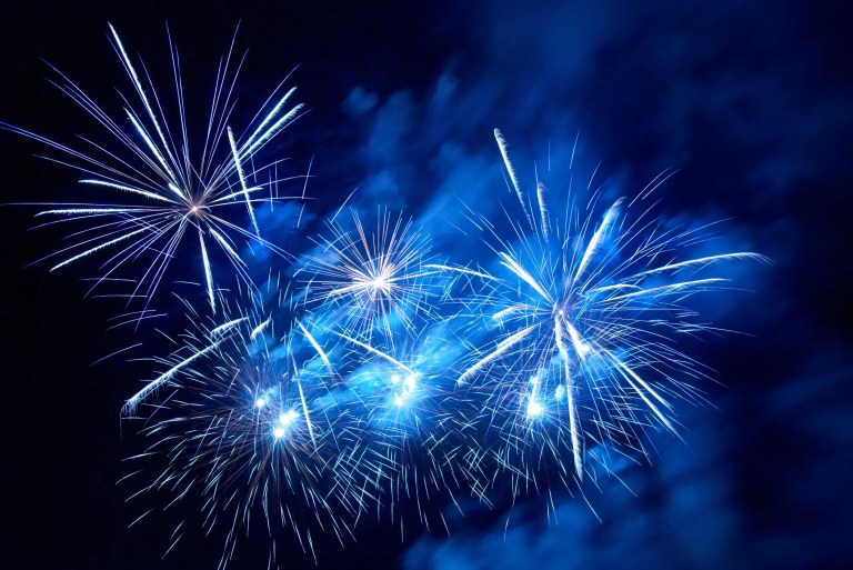White fireworks exploding on blue and black background.
