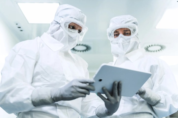 Two suited up cleanroom technicians covered in IEST-RP-CC003.4 attire.