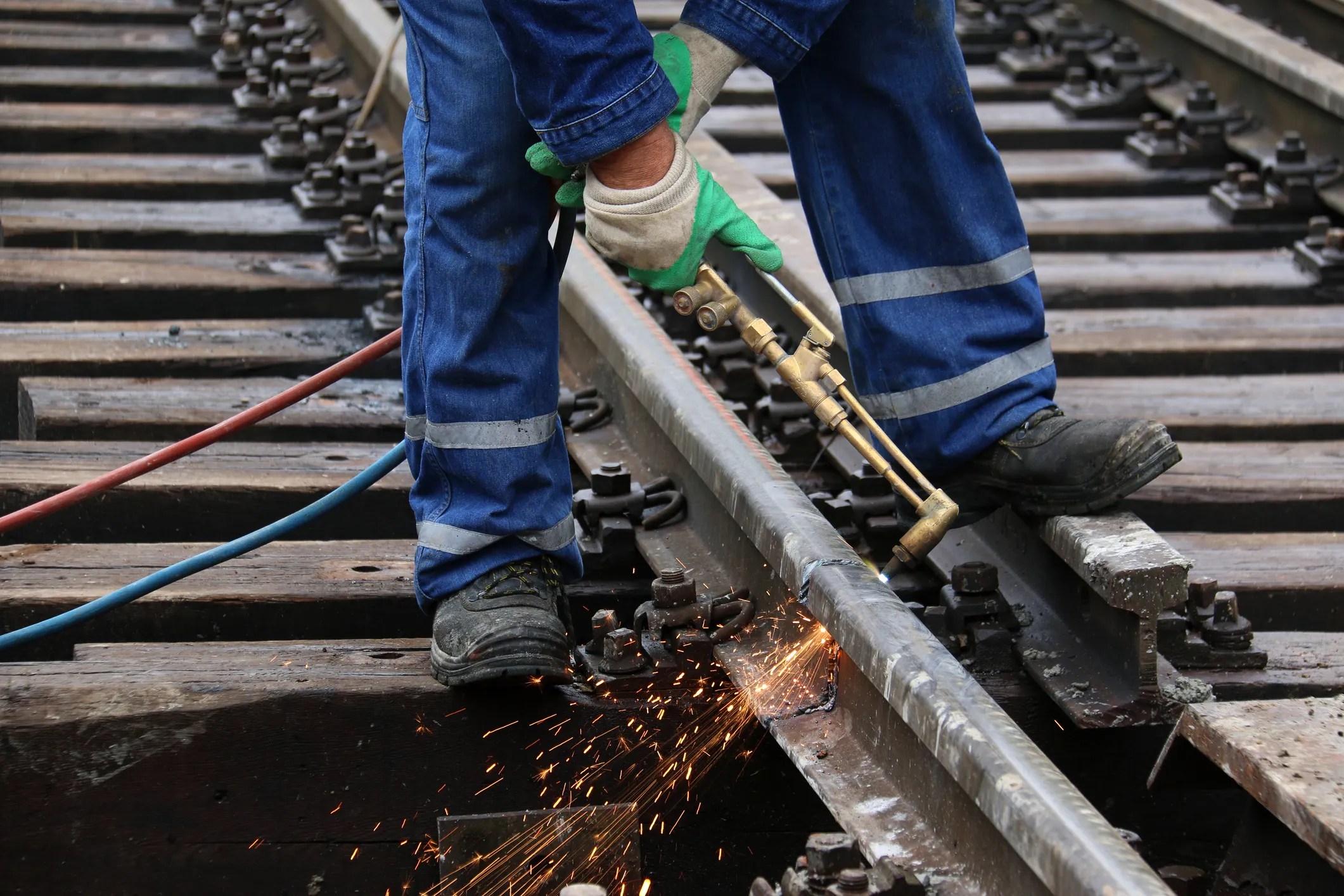 Welder in blue jumpsuit working on joining railroad track