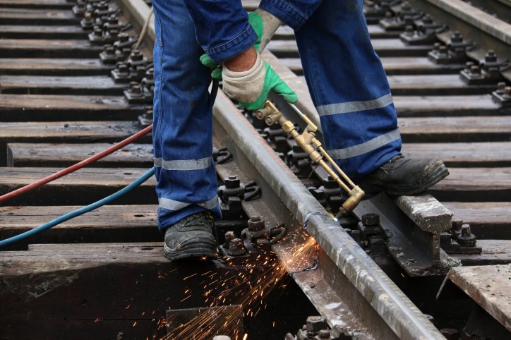 Welder in blue jumpsuit working on joining railroad track