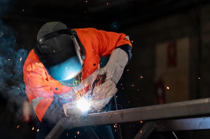 Welder in orange welding steel in dark room.