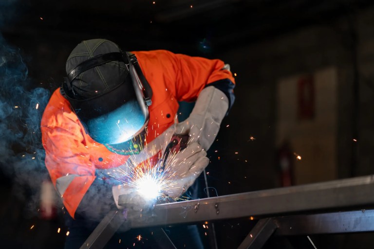 Welder in orange welding steel in dark room.