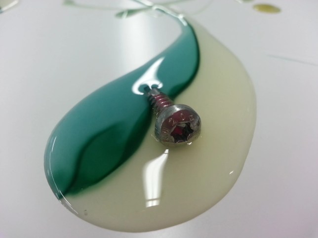 Screw floating in green and white adhesive glue.
