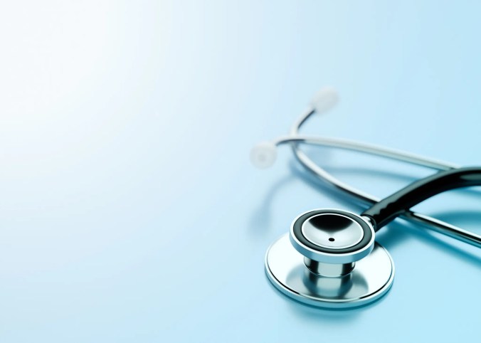 Stethoscope laying on light blue surface with ISO 9000 requirements.