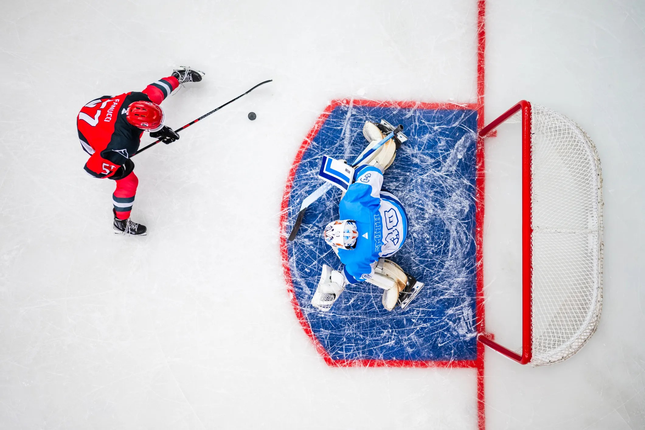 Red about to score hockey goal on blue goalie. Both are wearing CSA Z262.2-2015 masks.