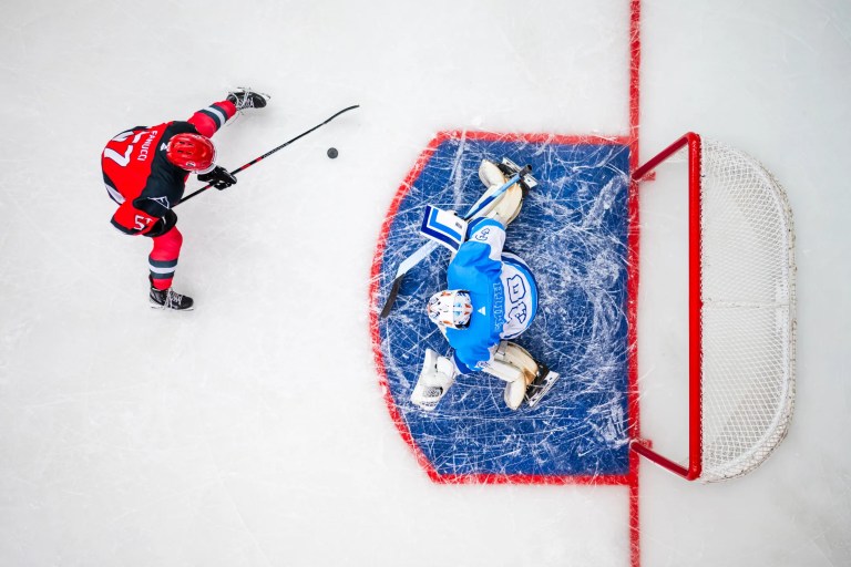 Red about to score hockey goal on blue goalie. Both are wearing CSA Z262.2-2015 masks.