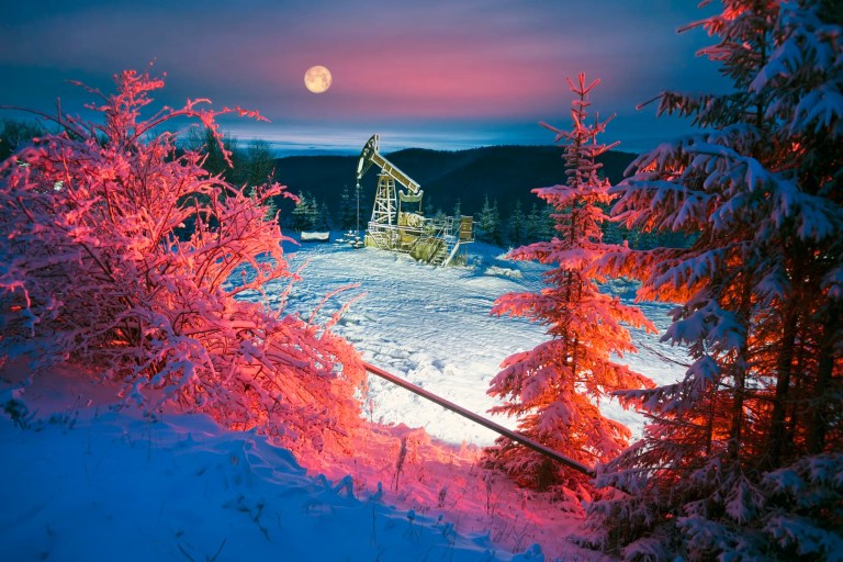 Pumpjack behind red evergreens in snow to show Oil production on Mount Synechka