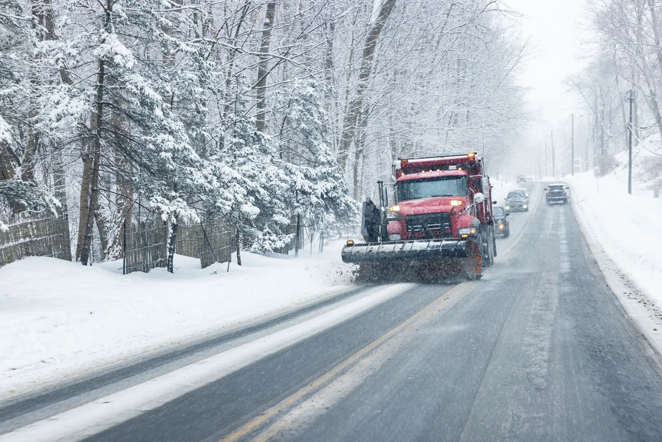 Snowplow clearing major road ahead of cars in winter Rochester, NY.