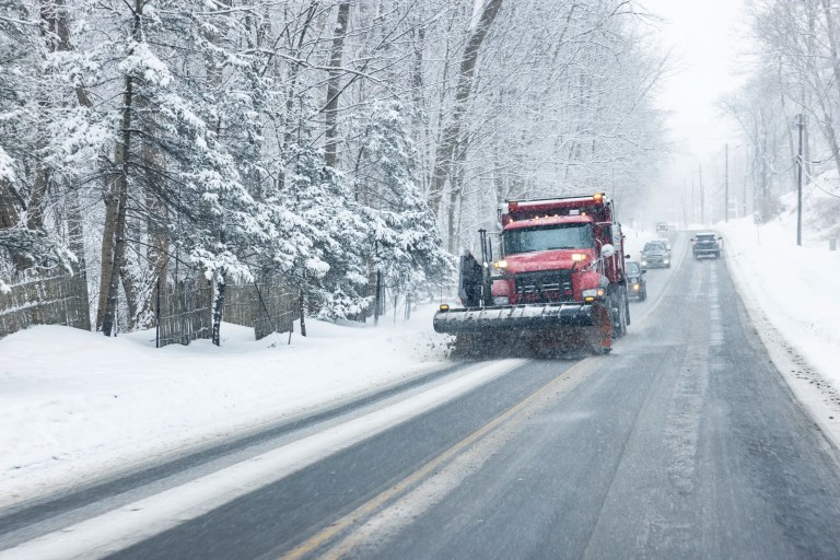 Snowplow clearing major road ahead of cars in winter Rochester, NY.