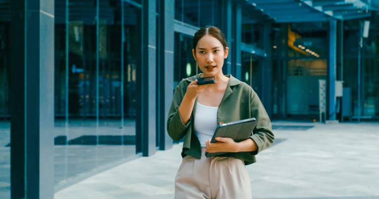 Woman speaking into phone near business to use speech to text technology