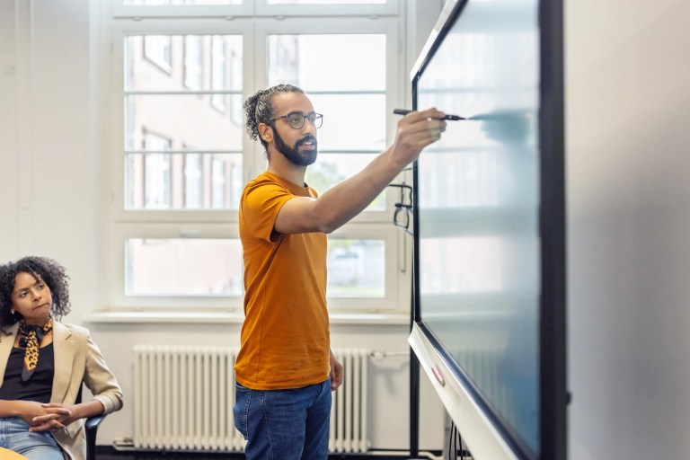 Young business leader in orange shirt writing on touch screen monitor