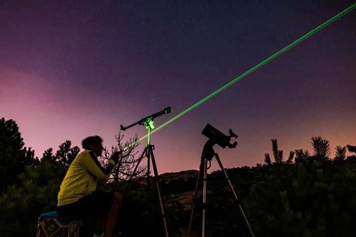 Green laser from telescope casting into the starry desert sky.