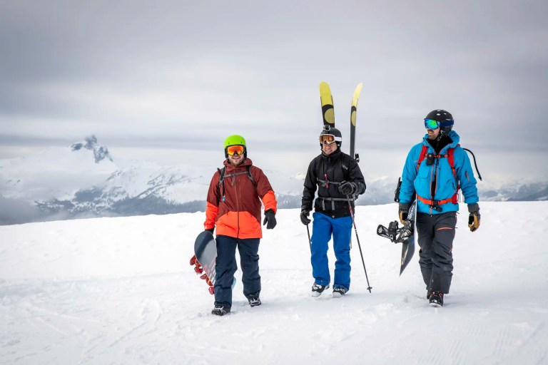 Two snowboarders walking with skiier carrying their equipment in snowy backcountry