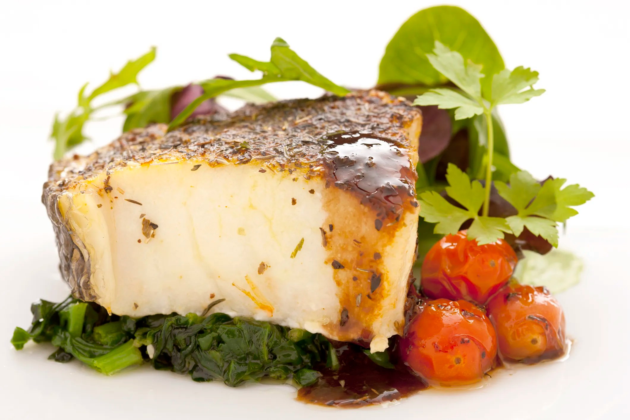 Chilean Sea Bass, or Patagonian Toothfish steak with a bite missing beside parsley, spinach, and red cherry tomatoes