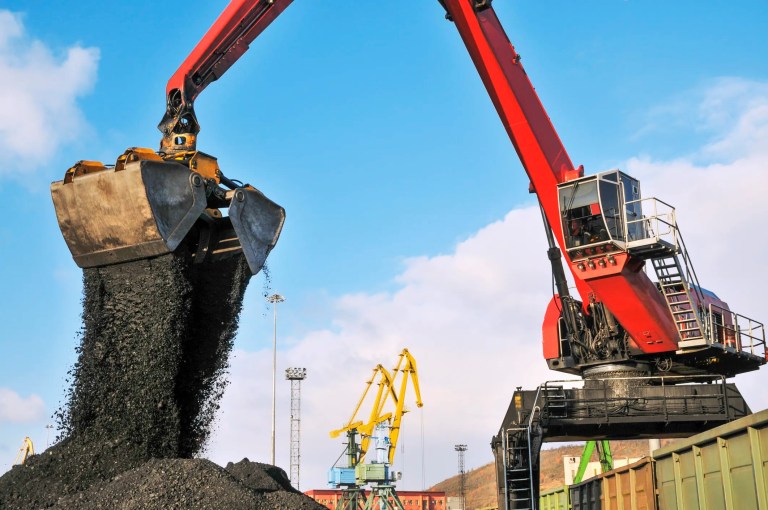 Red crawler hydraulic crane-manipulator unloads coal from wagons and lets it fall to ground