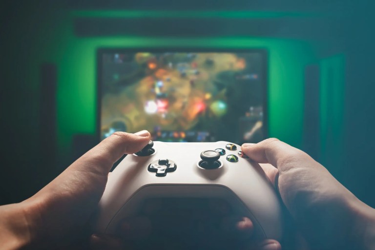 Playing white Xbox controller with multiplayer online battle arena game on TV