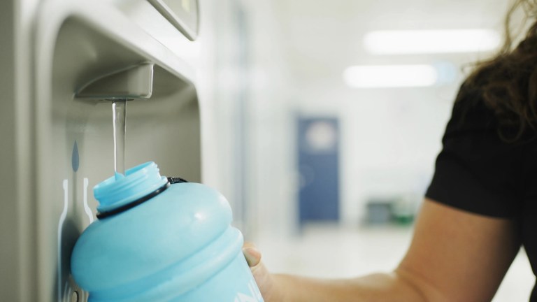 Teacher refilling water bottle at fountain in hallway