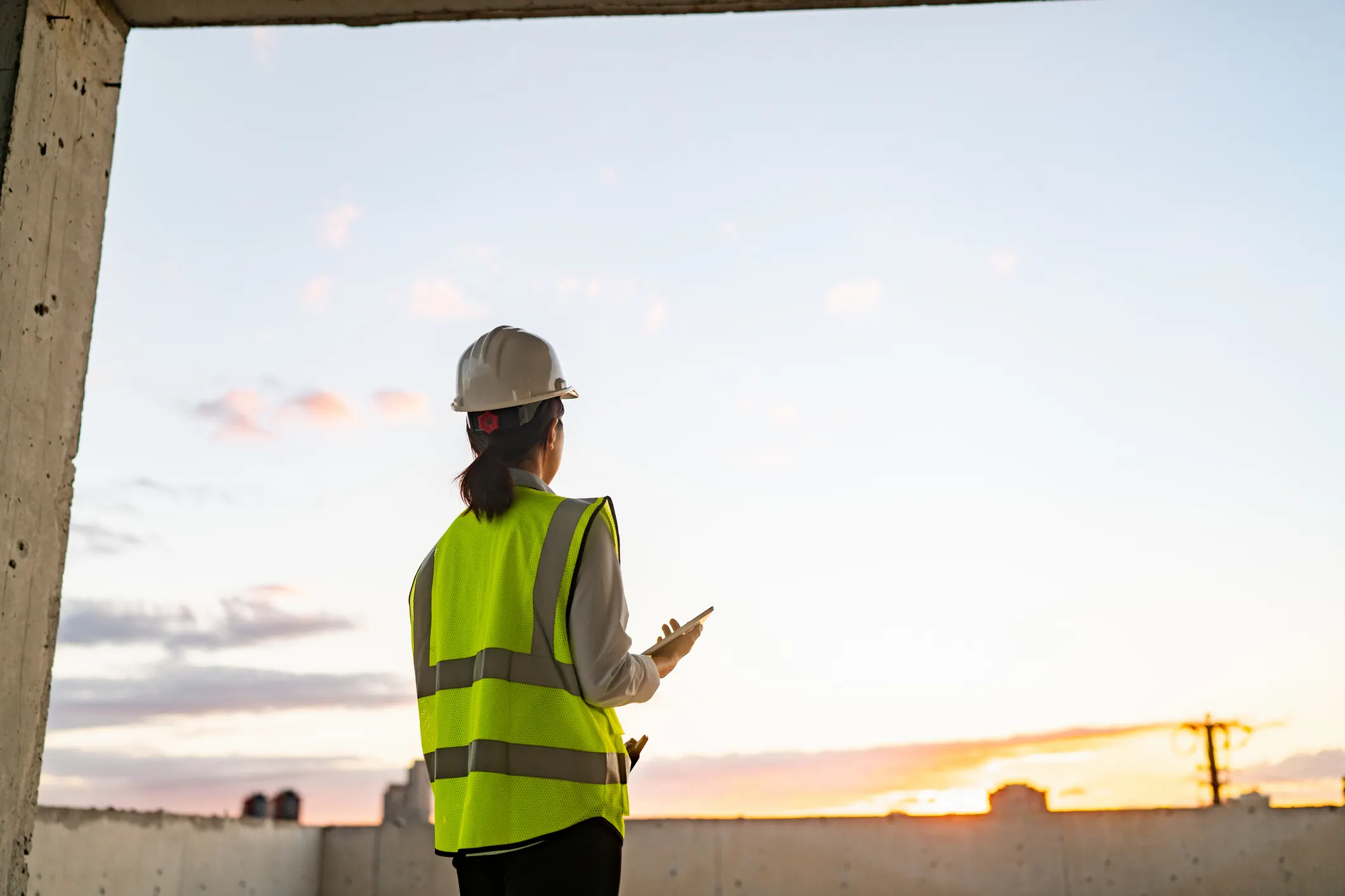 Woman in yellow HVSA wearing white ANSI Z89.1 hardhat and staring into sky