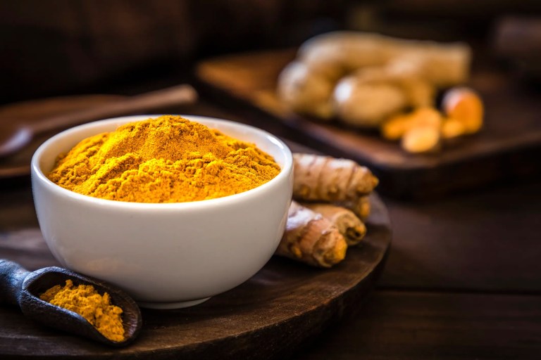 Colorful turmeric in white bowl beside turmeric roots