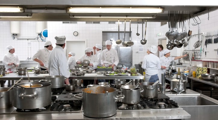 Chefs preparing dinner for patrons in bustling ANSI Z83.11-2025 kitchen.