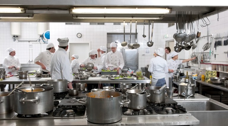 Chefs preparing dinner for patrons in bustling ANSI Z83.11-2025 kitchen.