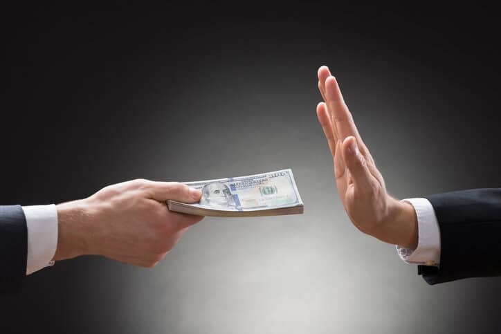Businessman hand rejecting cash bribe from other hand after reading ISO 37001:2025 anti-bribery management systems.