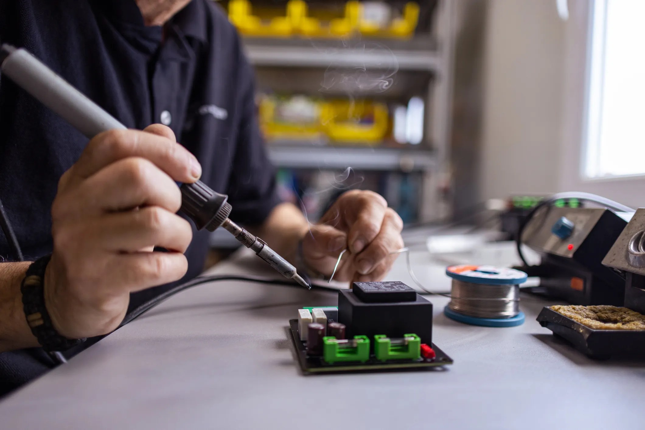 A soldering technician in a lab wearing ESD wrist strap as smoke rises from circuit board.