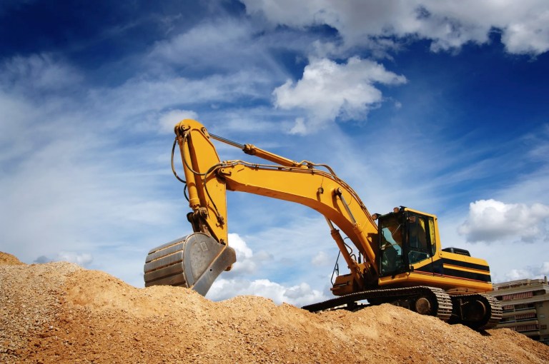 An ISO 14990-1 excavator moving dirt at work site beneath clouded blue sky