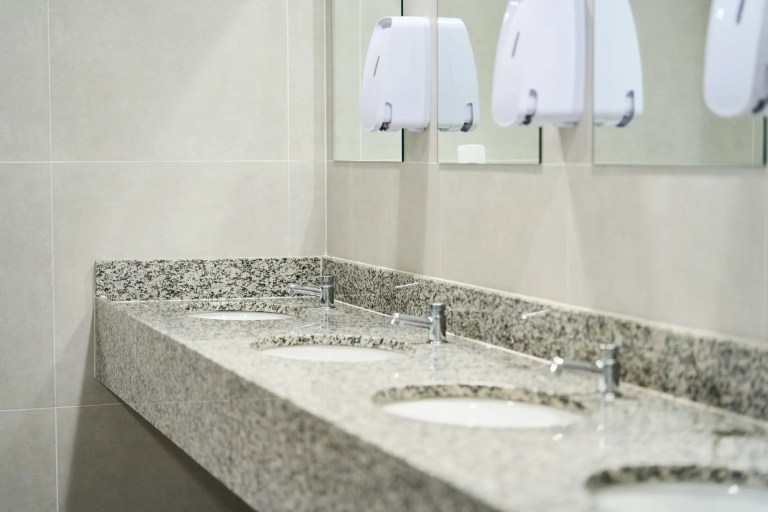Sinks lined up on granite in ANSI/PSAI Z4.1-2016 workplace bathroom