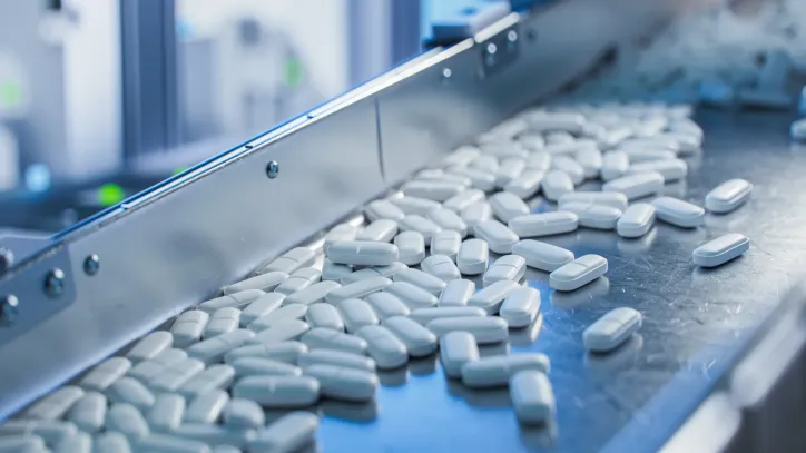 White pills moving along chrome conveyor to follow NSF/IPEC/ANSI 363-2024 GMP.