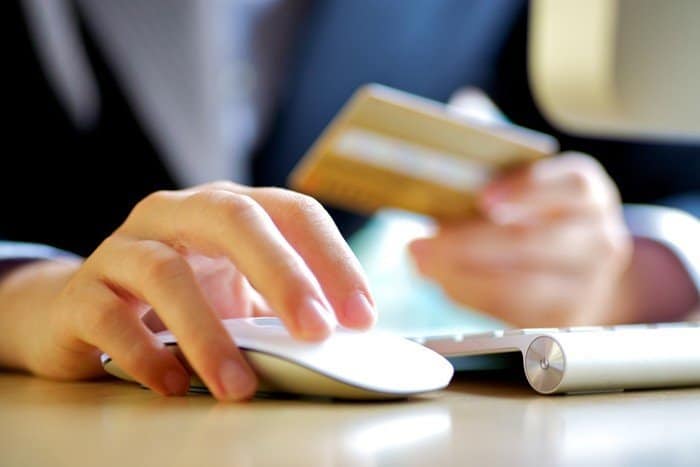 Someone clicking on a computer mouse while holding a credit card to demonstrate the guidelines set in ANSI X9.24-1