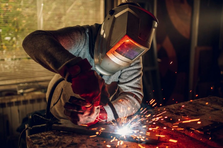 Welder working in front of window in metric units with red sparks flying