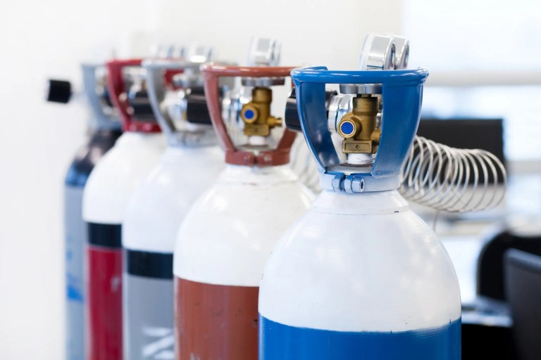 Lineup of red and blue CGA P-20-2017 compressed gas cylinders