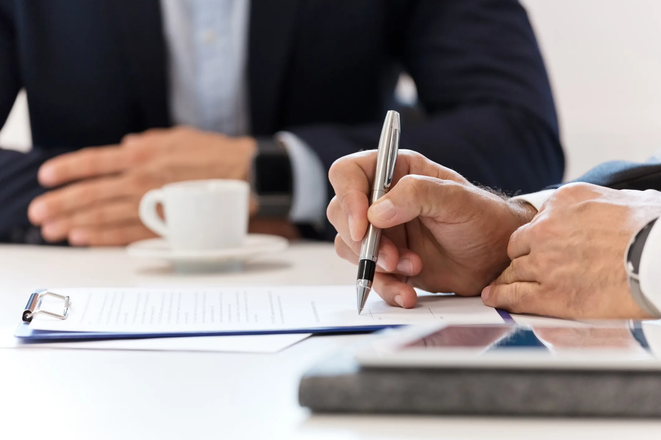 Two people in business suits writing an ISO amendment by hand in boardroom.