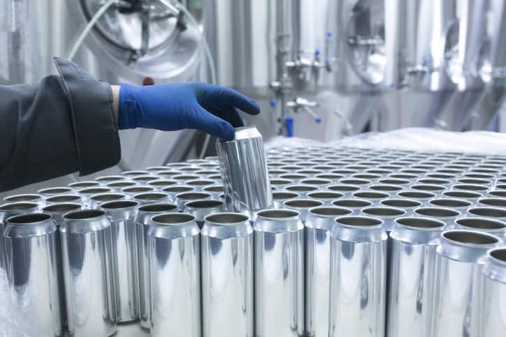 Aluminum beer cans being lifted by worker in blue glove after production in ANSI H35.2-2024 mill.