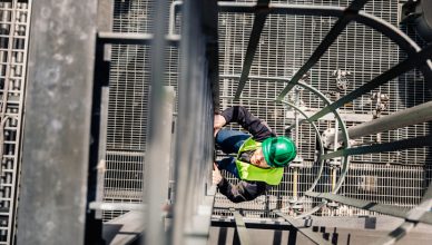 Man climbing a caged ladder while donning ANSI/ISEA 107-2020 High-Visibility Safety Apparel.