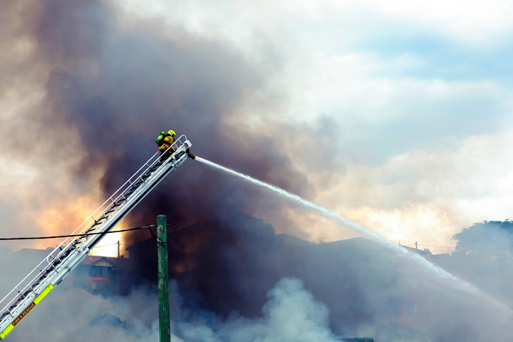 Firefighter on a ladder with water hose trying to control a fire by following NFPA Fire Code 1 2018