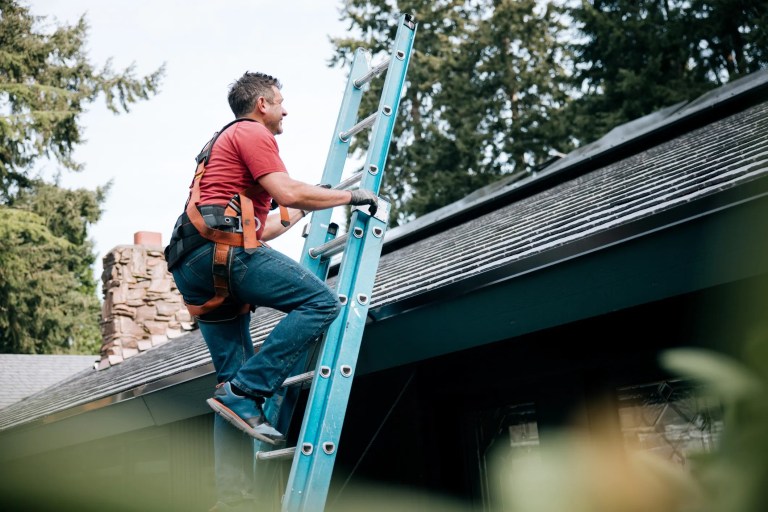 Man climbing blue ladder to install solar panels on house in Washington