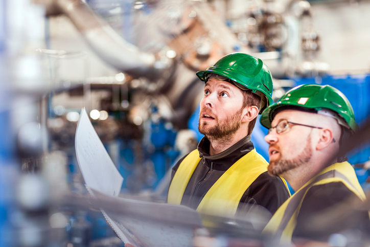 Two managers donning green hardhats conduct ISO 45001 continual improvement.