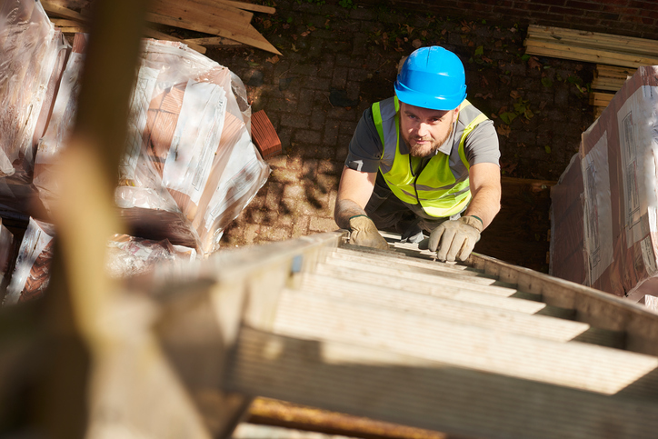 Man working hard on wooden ladder to not become an accident statistic, according to ALI and Ladder Safety Month
