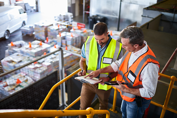 Two warehouse managers reviewing ANSI standards and OSHA requirements for warehouse safety.