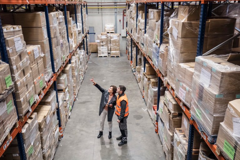 Two auditors pointing toward warehouse boxes with ISO 19011 guidance