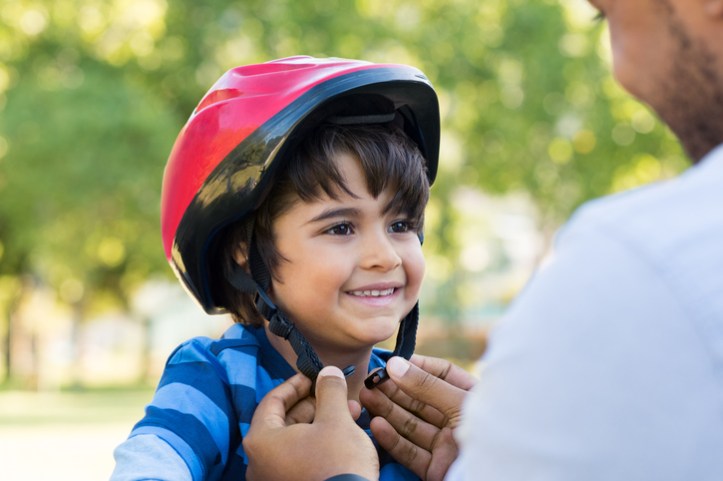 Father tightening red ASTM F1447-18 bicycle helmet on happy son's head.