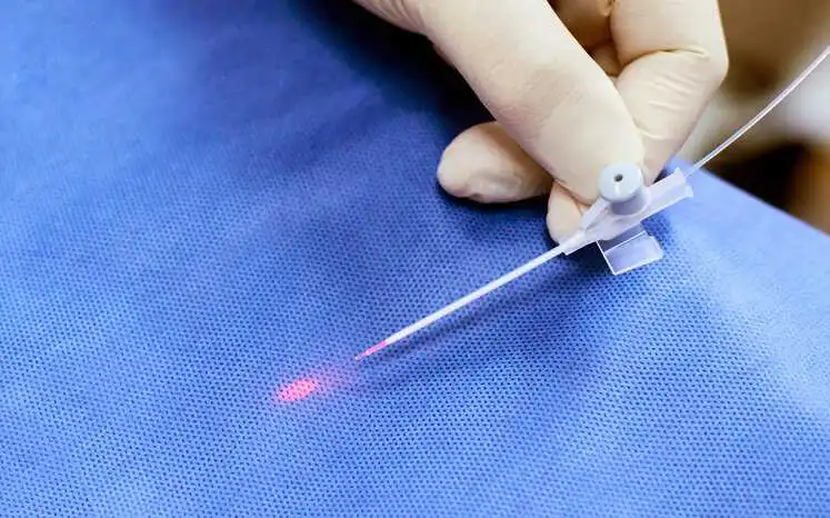 Red laser being used over blue gown to remove varicose vein in healthcare facility