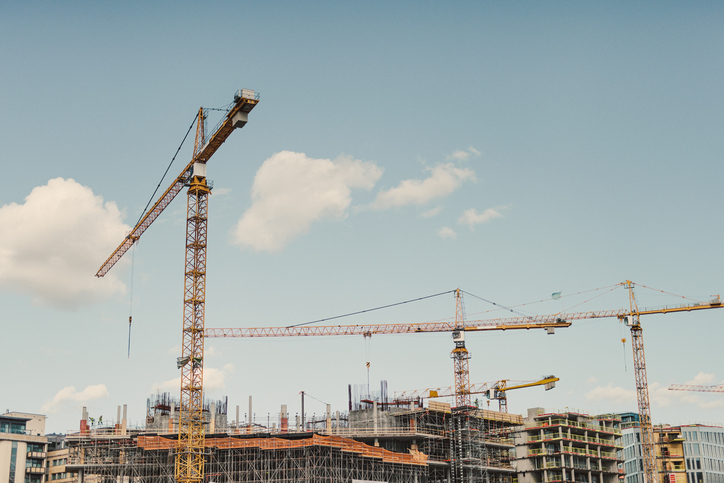 Three cranes next to a construction site following OSHA standards