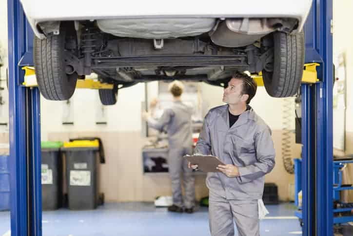 Auto mechanic in gray jumpsuit checking out car and depending on the AIAG CQI-20:2018 Problem Solving Guideline.