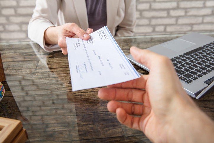 Woman handing an endorsed check to banker to efficiently transfer money with ANSI X9.100-111-2018.