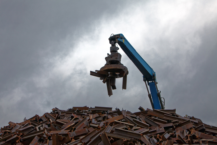 A blue ASME B30.25-2018 machine handling scrap in a junkyard.
